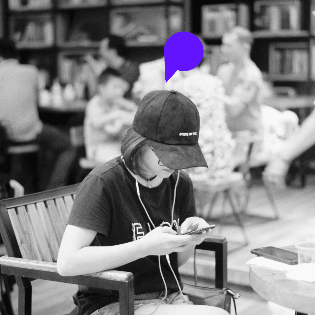 Femme avec une casquette, confortablement installée sur un banc dans un lieu public, plongée dans l’écoute d’un podcast sur son téléphone.